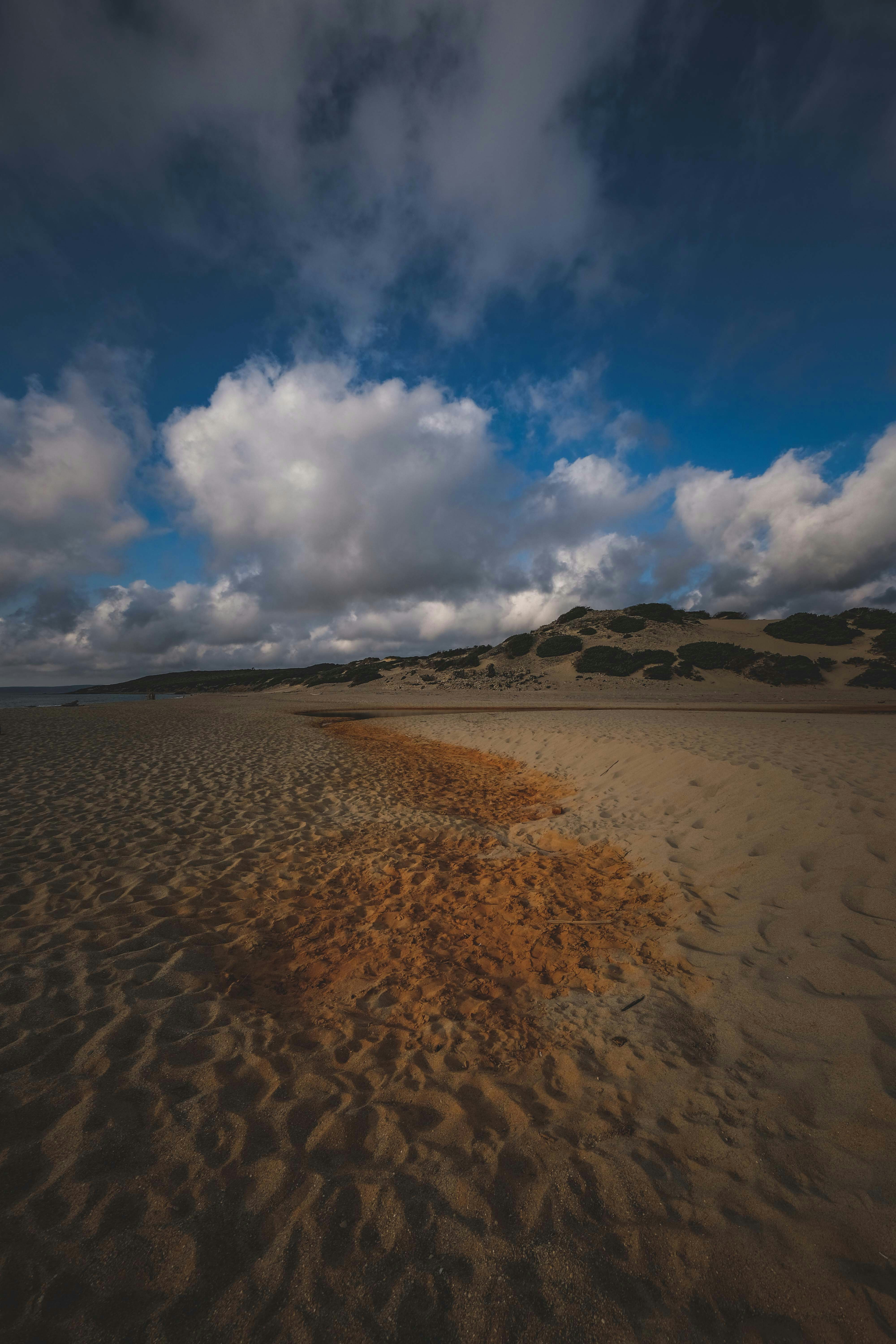 brown sand under white clouds and blue sky during daytime